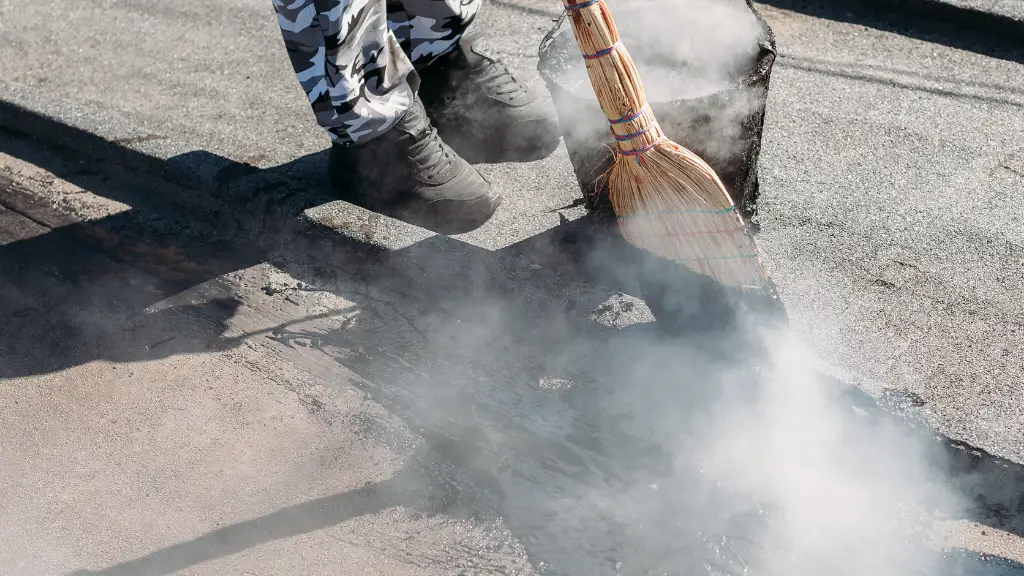 Worker repairs the roof with molten tar from a bucket with a broom. Roof repair tar.