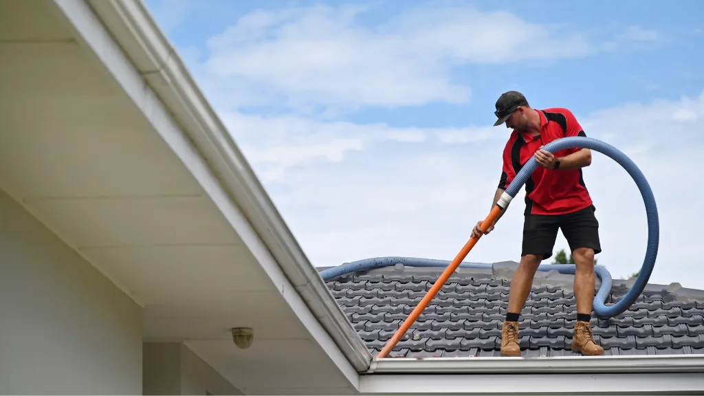 Roofer using a blower to clean gutters of debris. 